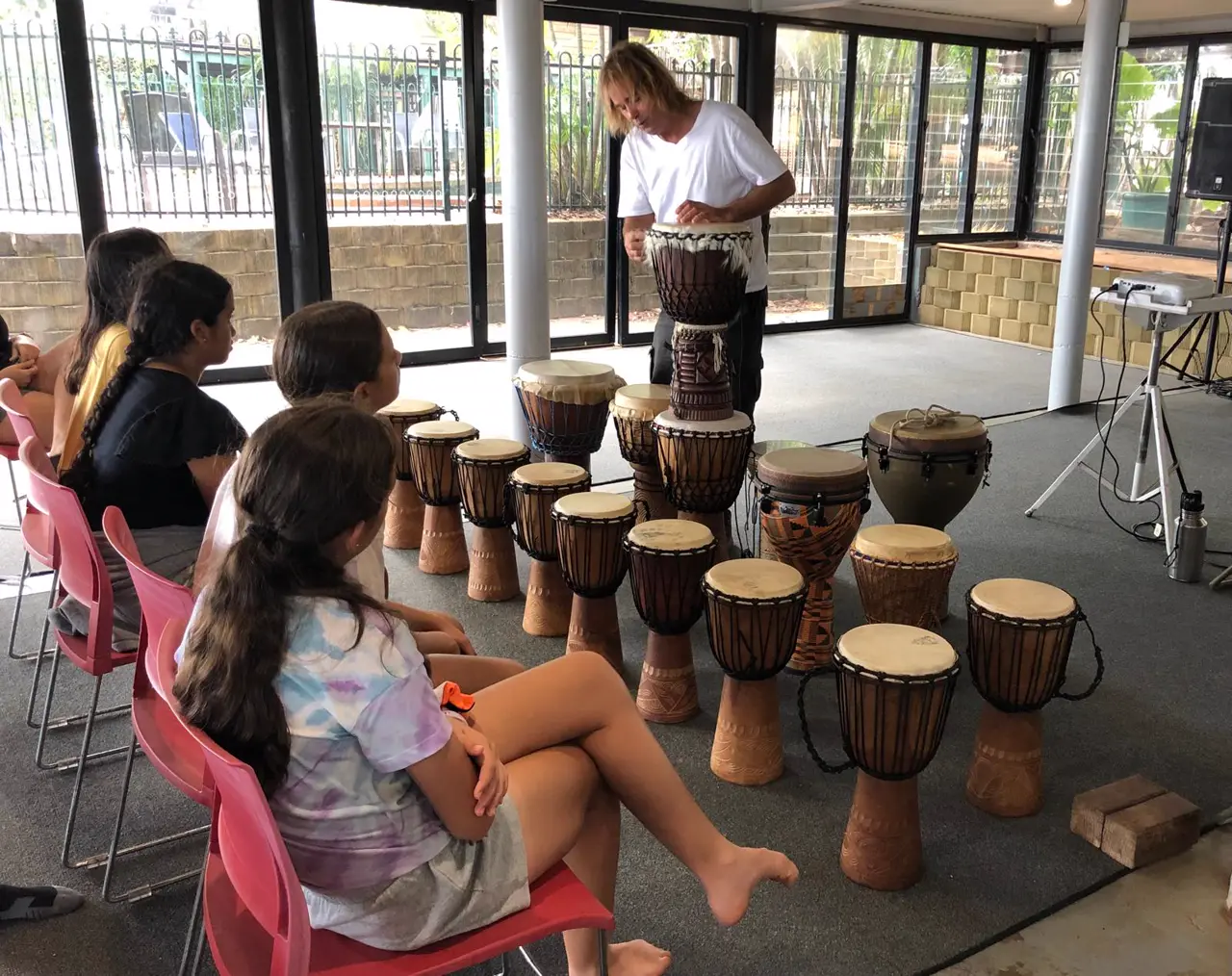 Colin demonstrating a djembe to a group of students with a row of drums ready
