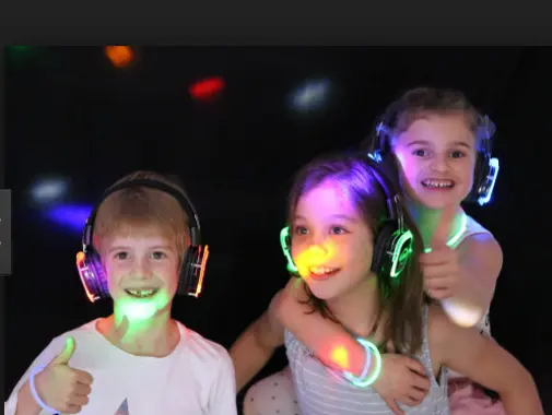 Three children wearing glowing silent disco headphones
